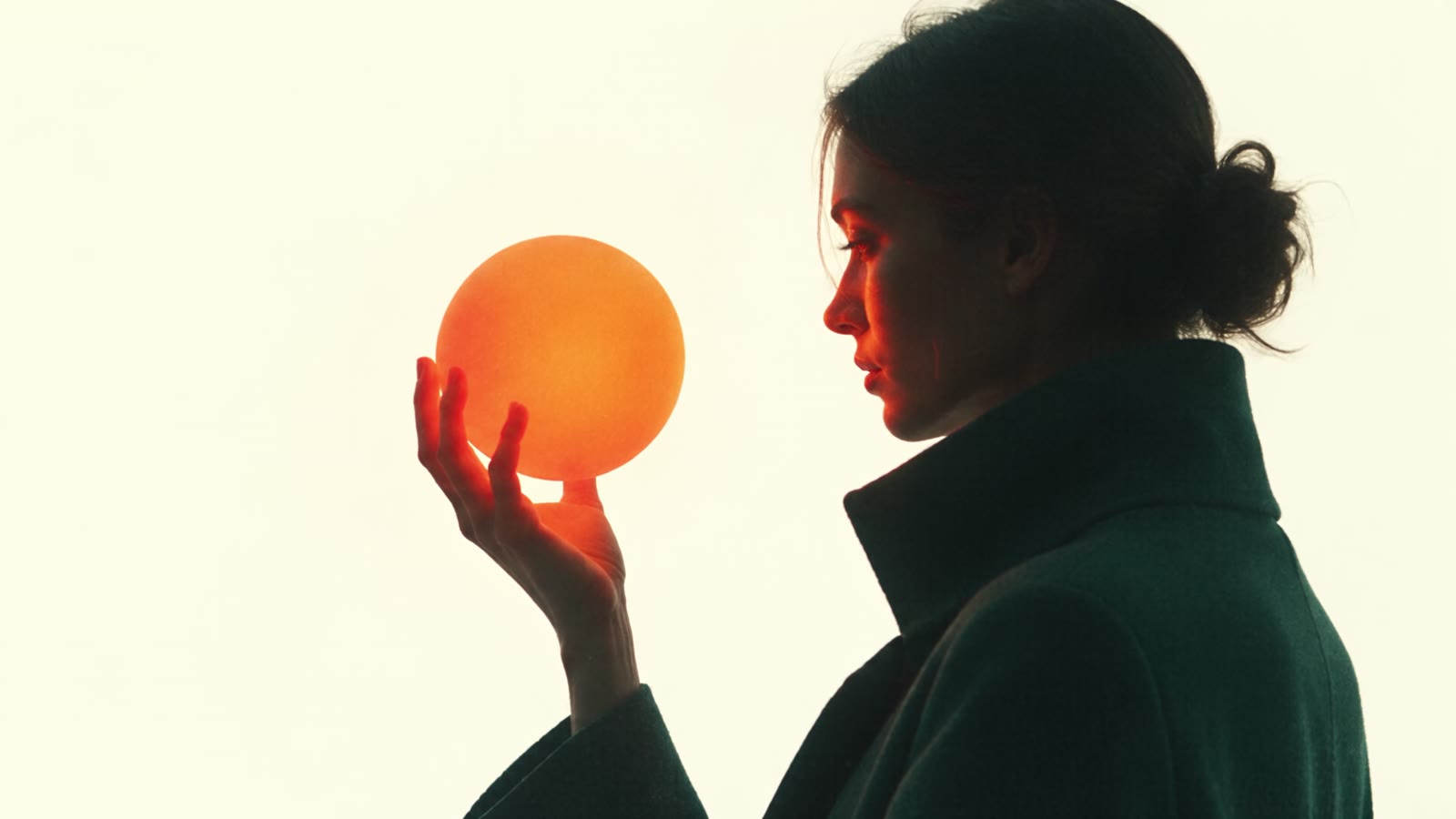 A figure in a green coat holding a glowing orange sphere